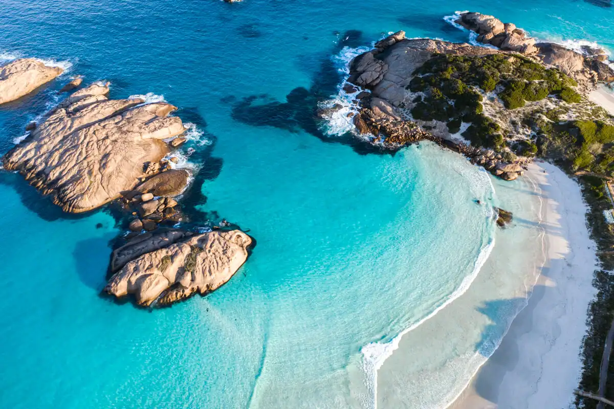Aerial view of turquoise water, sandy beach, and large rocky formations along the coastline.