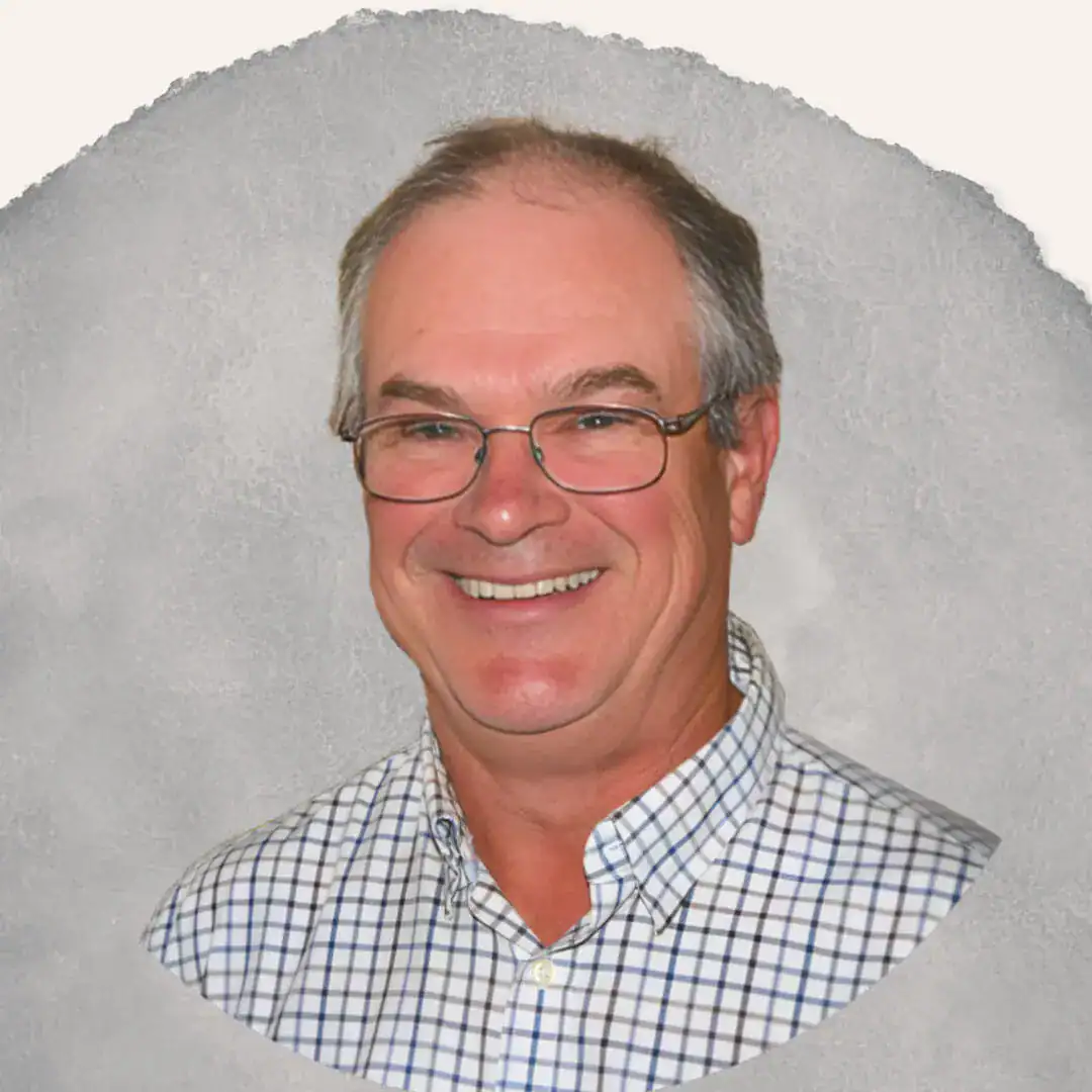 Smiling older man with glasses and gray hair, wearing a checkered shirt, in front of a gray background.