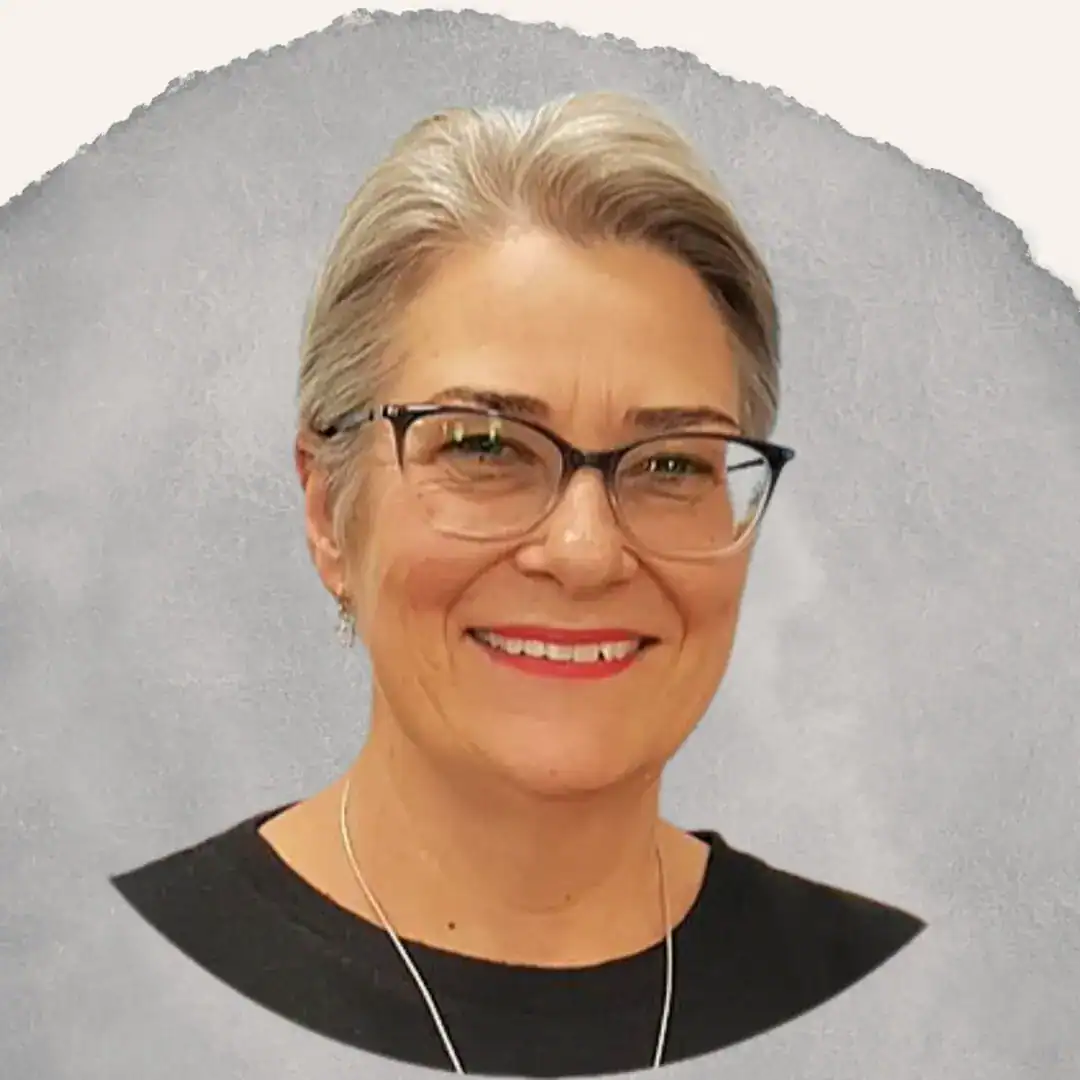Smiling woman with short gray hair, glasses, and a black top against a soft gray background.