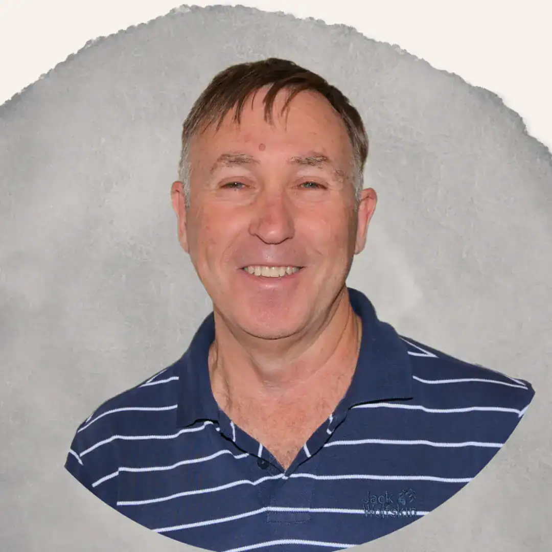 Smiling man with short brown hair wearing a navy blue and white striped collared shirt on a gray background.